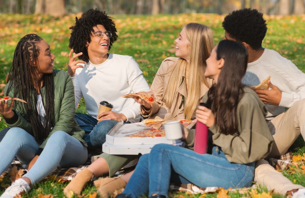 Cheerful closed friends having fun at park, eating pizza