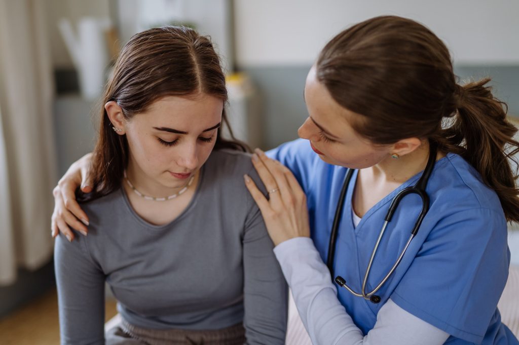 Young nurse taking care of teenage girl, consoling her.